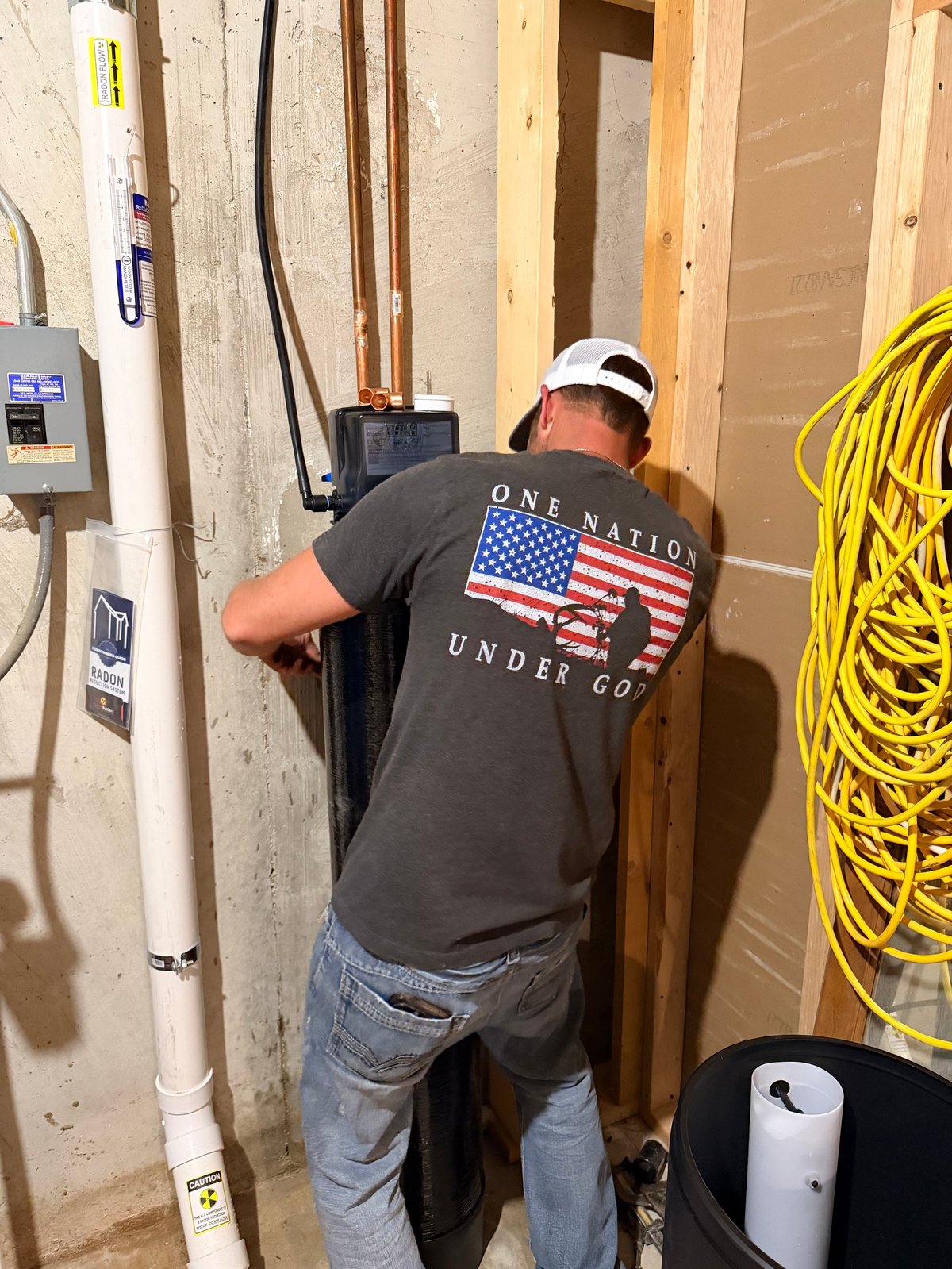 Construction worker in white hard hat installing electrical wiring in unfinished interior wall with wooden framing and yellow cable visible