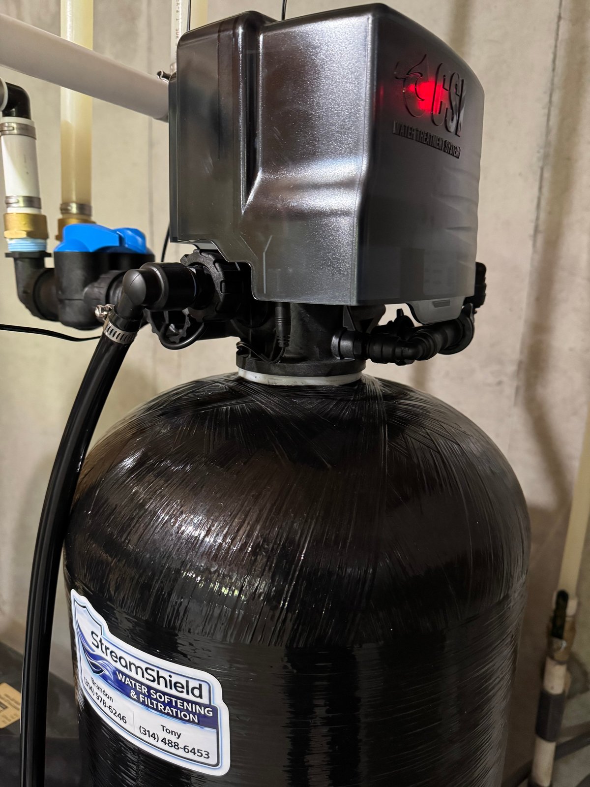 Water softener system with black tank and control valve head featuring blue handles and red indicator light