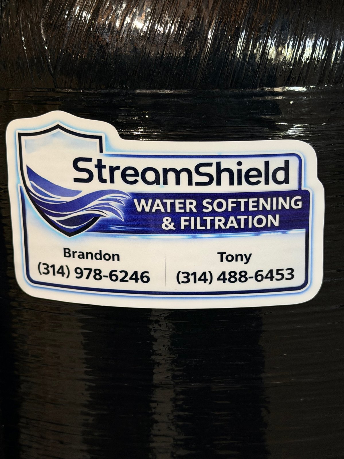 StreamShield water softening and filtration business card with contact numbers for Brandon and Tony on textured black background