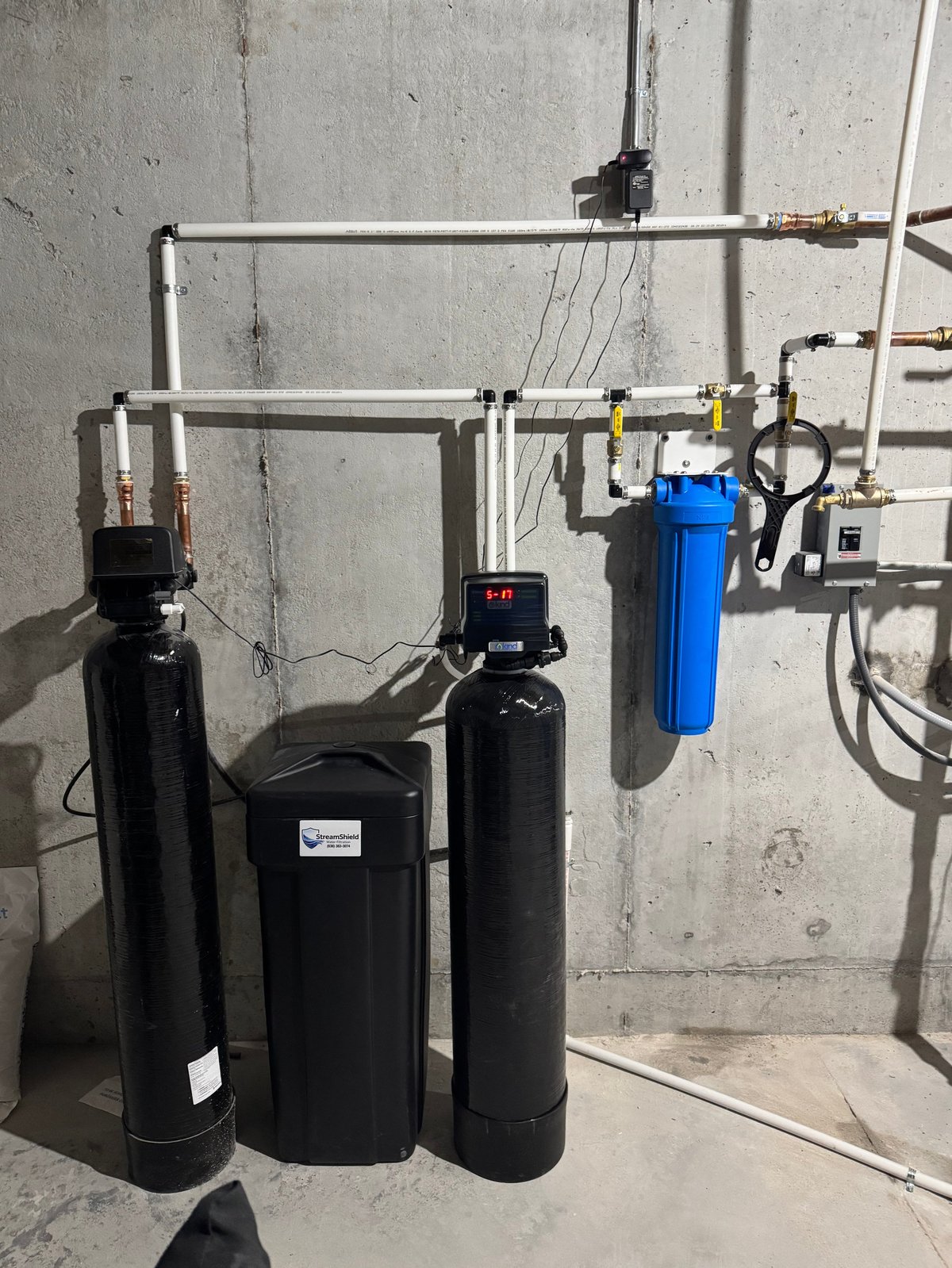 Water treatment system with black cylindrical tanks and blue filter cartridge mounted on concrete wall