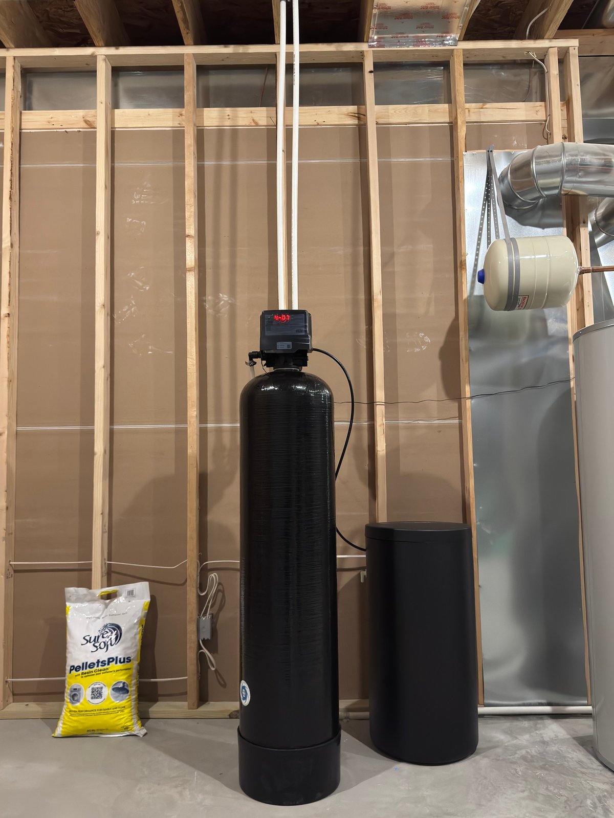 Black water softener tank system with electronic control valve in a utility room with plastic sheeting and construction materials